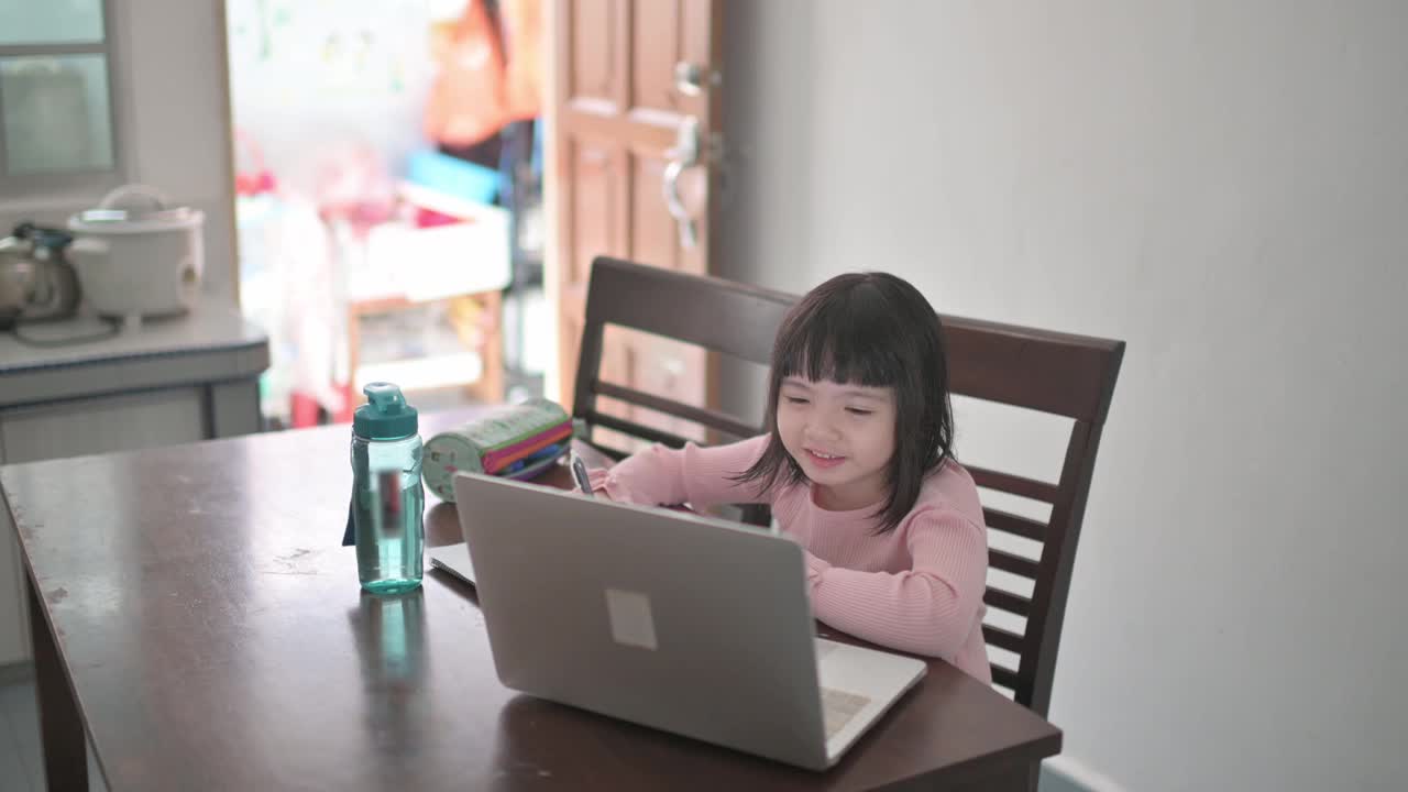 亚裔中国女孩在她姐姐的帮助下在厨房餐桌上参加网络课程视频素材