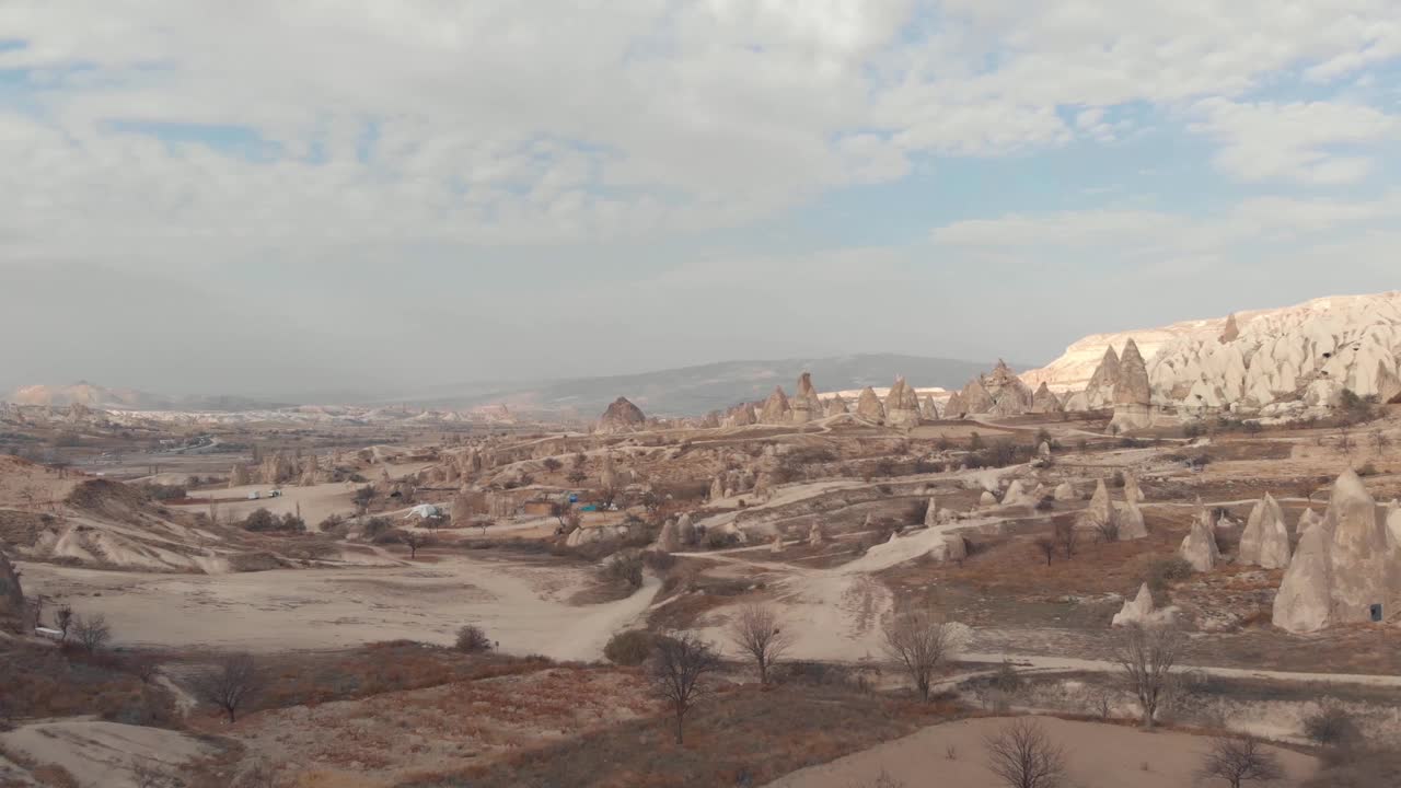 崎岖贫瘠的景观点缀着仙女般的烟囱，在卡帕多西亚，土耳其-低角度飞行鸟瞰图视频素材