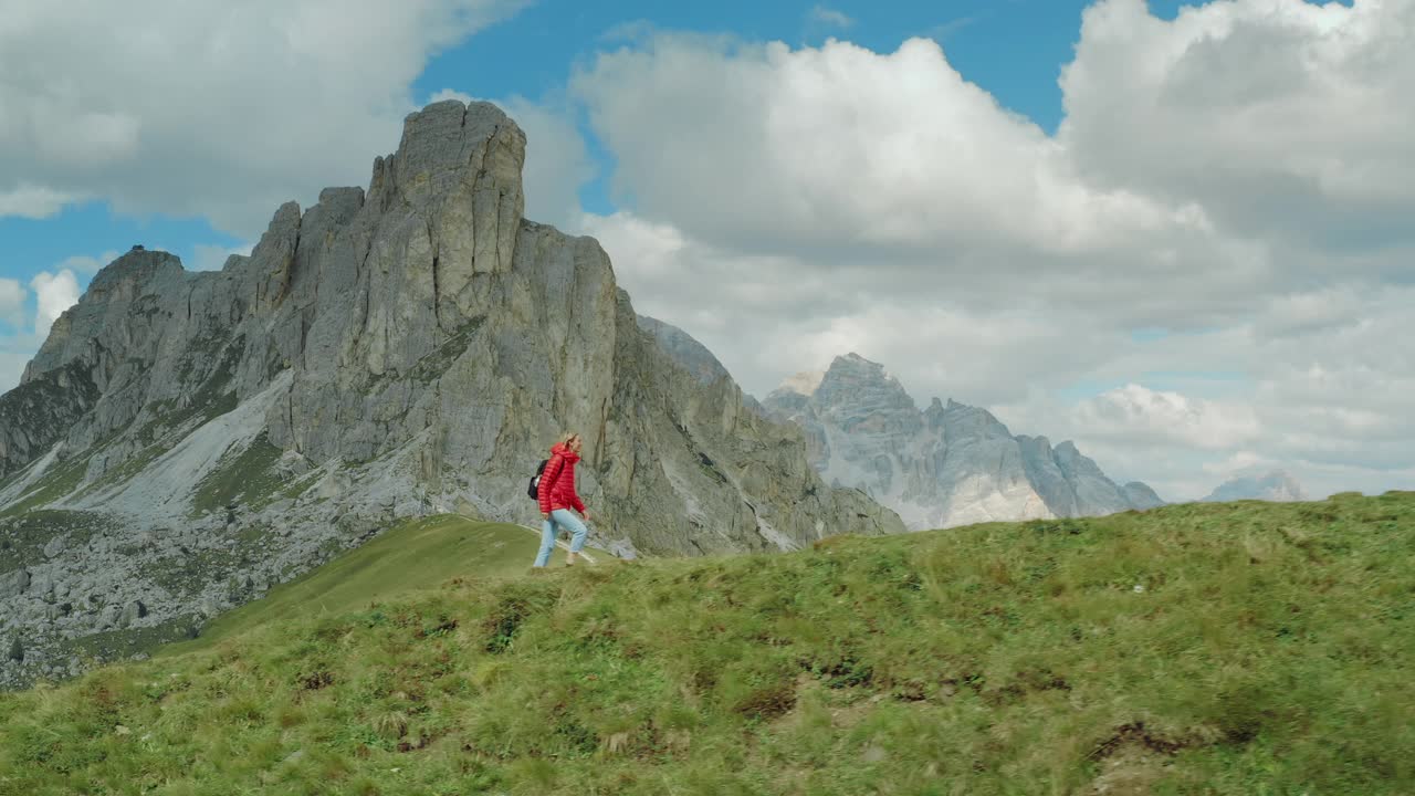 鸟瞰图的一个年轻快乐的女游客在一个风景如画的Dolomites徒步旅行在一个阳光明媚的日子俯瞰Passo Giau的空小径。视频素材