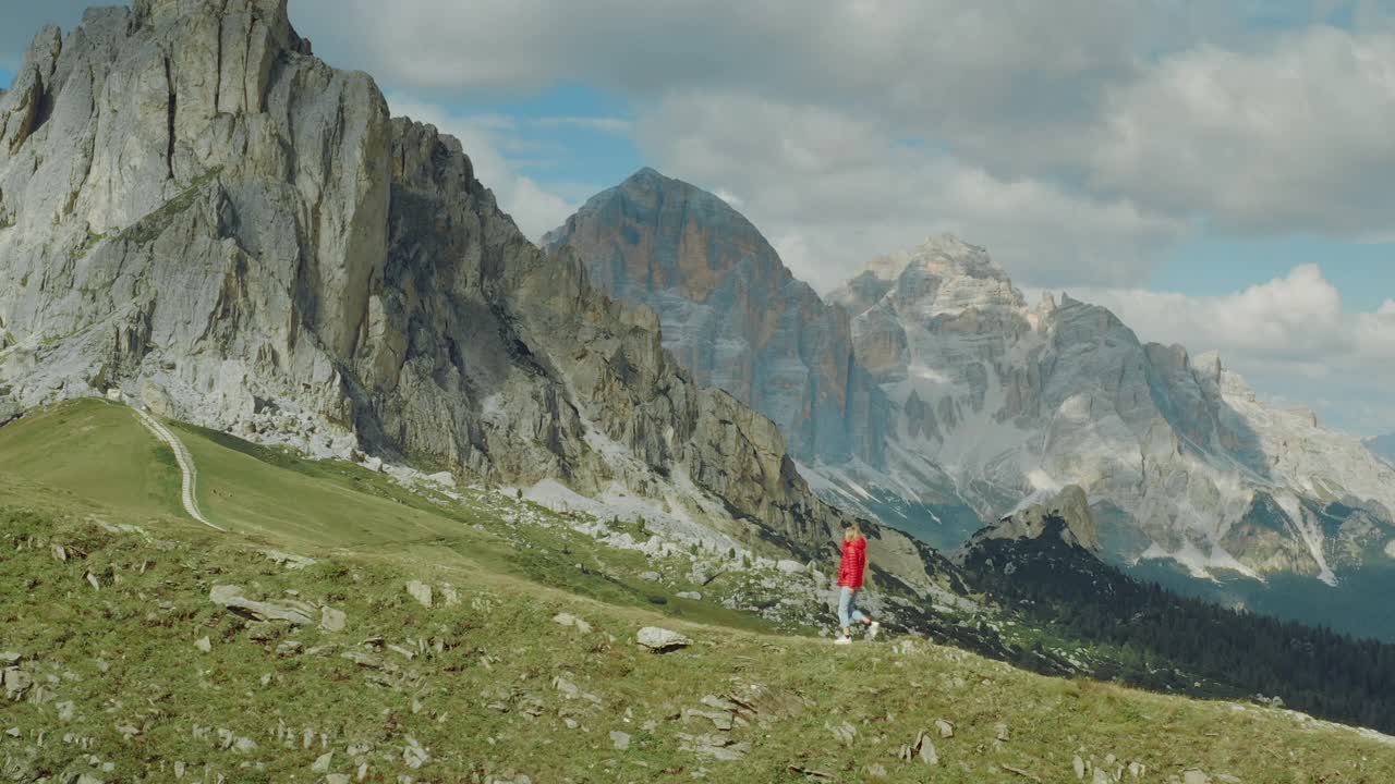 鸟瞰图的一个年轻快乐的女游客在一个风景如画的Dolomites徒步旅行在一个阳光明媚的日子俯瞰Passo Giau的空小径。视频素材