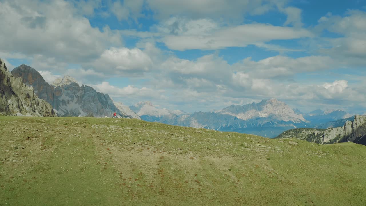 年轻的女性徒步旅行者在风景如画的多洛米特的一条空旷小径上奔跑。穿着红夹克的女游客沿着帕索焦山附近的一条山路慢跑。旅行者在意大利和奥地利的阿尔卑斯山徒步旅行。视频素材