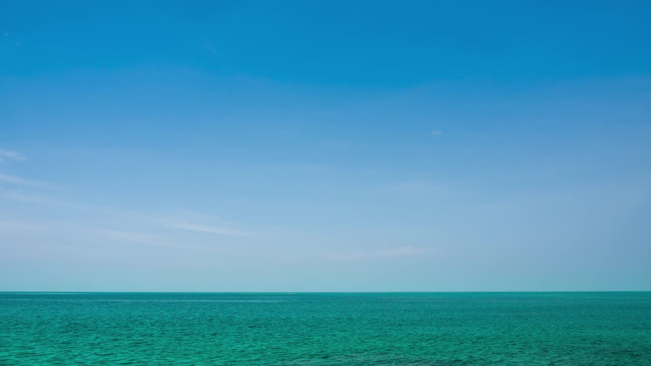 平静的海浪的时间推移镜头，海洋在一个晴朗的日子与柔和的蓝色梯度和薄云透明的天际线。阳光反射在海面上。B卷视频海背景视频素材