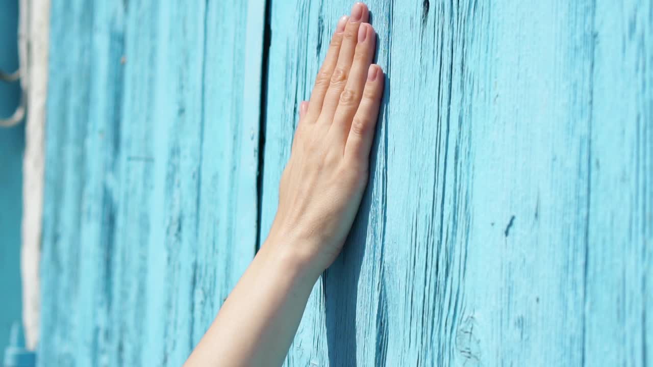 女人的手缓慢地靠在蓝色的木门上。女性手触摸表面的木材视频素材