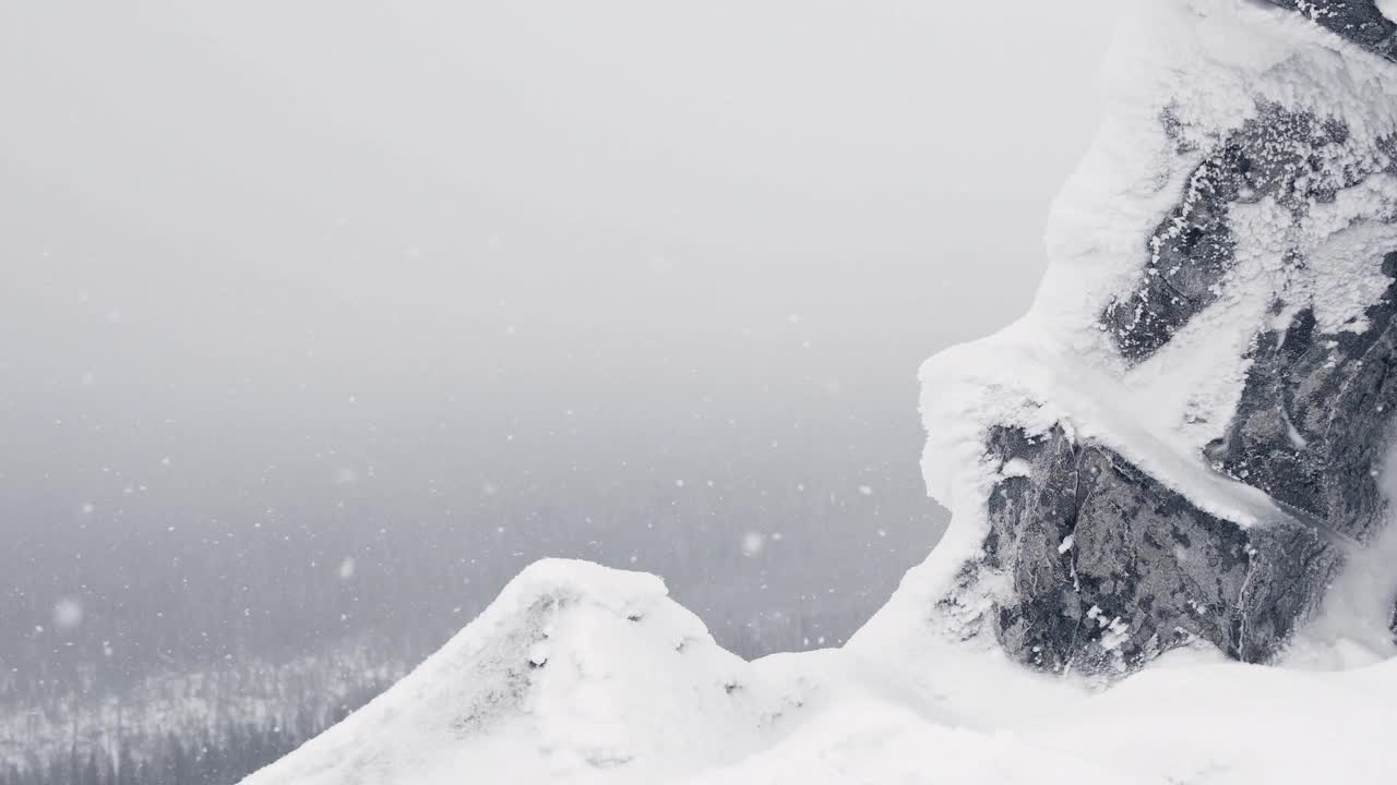 落雪在岩石山顶。悬崖上覆盖着冰和霜。穿过雪花飘落的冬日森林。树顶上方有雾和用于文本的自由空间视频素材