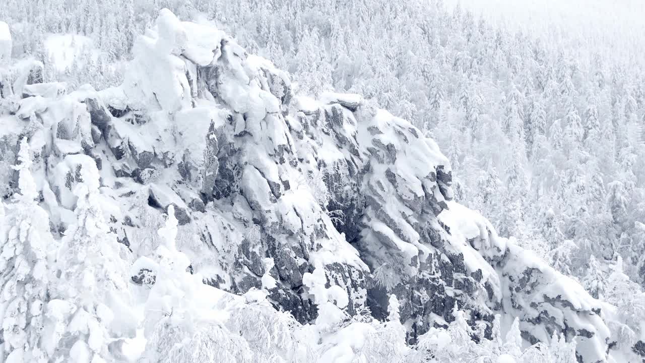 寒冷的日子，山坡上下雪。冬季的景观是被冷杉包围的冰冻岩石。雪花轻柔地落在岩石和蓬松的树枝上。悬崖上的雪堆和锋利的石头清晰可见视频素材