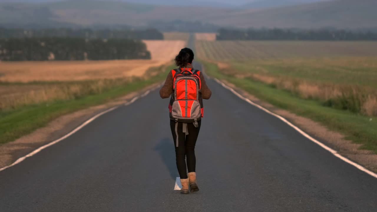 搭便车的旅行者女人与背包行走在农村的道路在日落视频素材