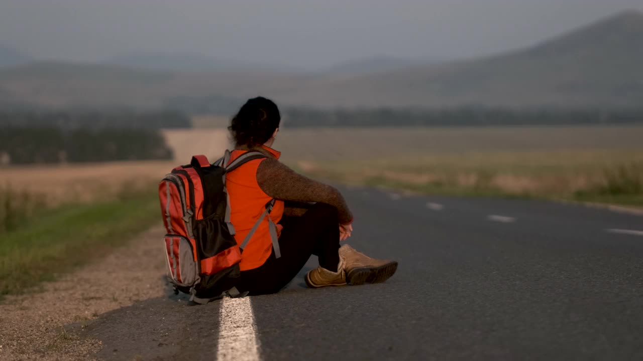 旅行者女人女孩坐在背包看地图在夏天的道路与过往的汽车视频素材