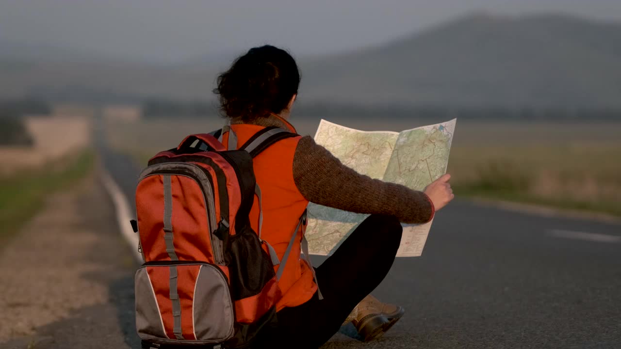 旅行者女人女孩坐在背包看地图在夏天的道路与过往的汽车视频素材