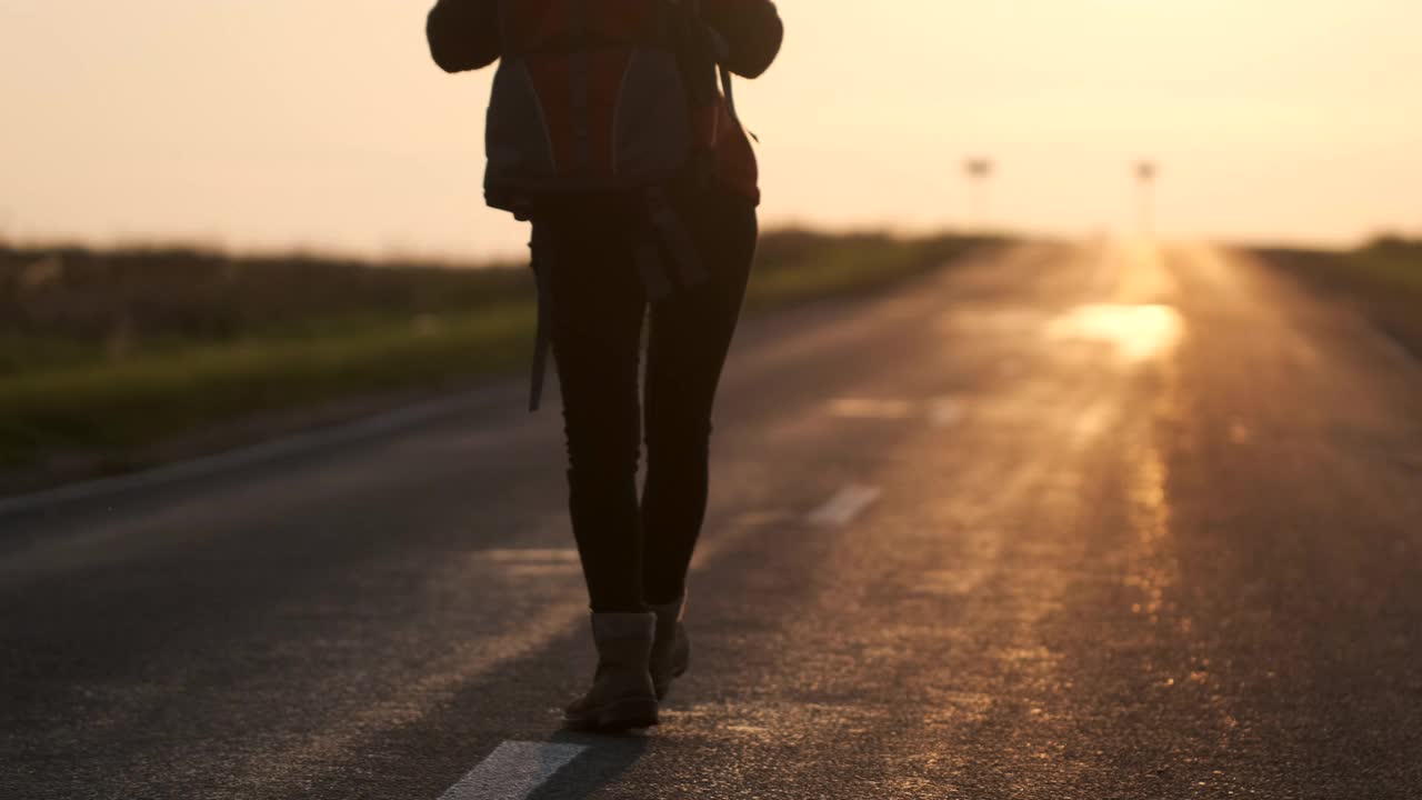 搭便车的旅行者女人与背包行走在农村的道路在日落视频素材