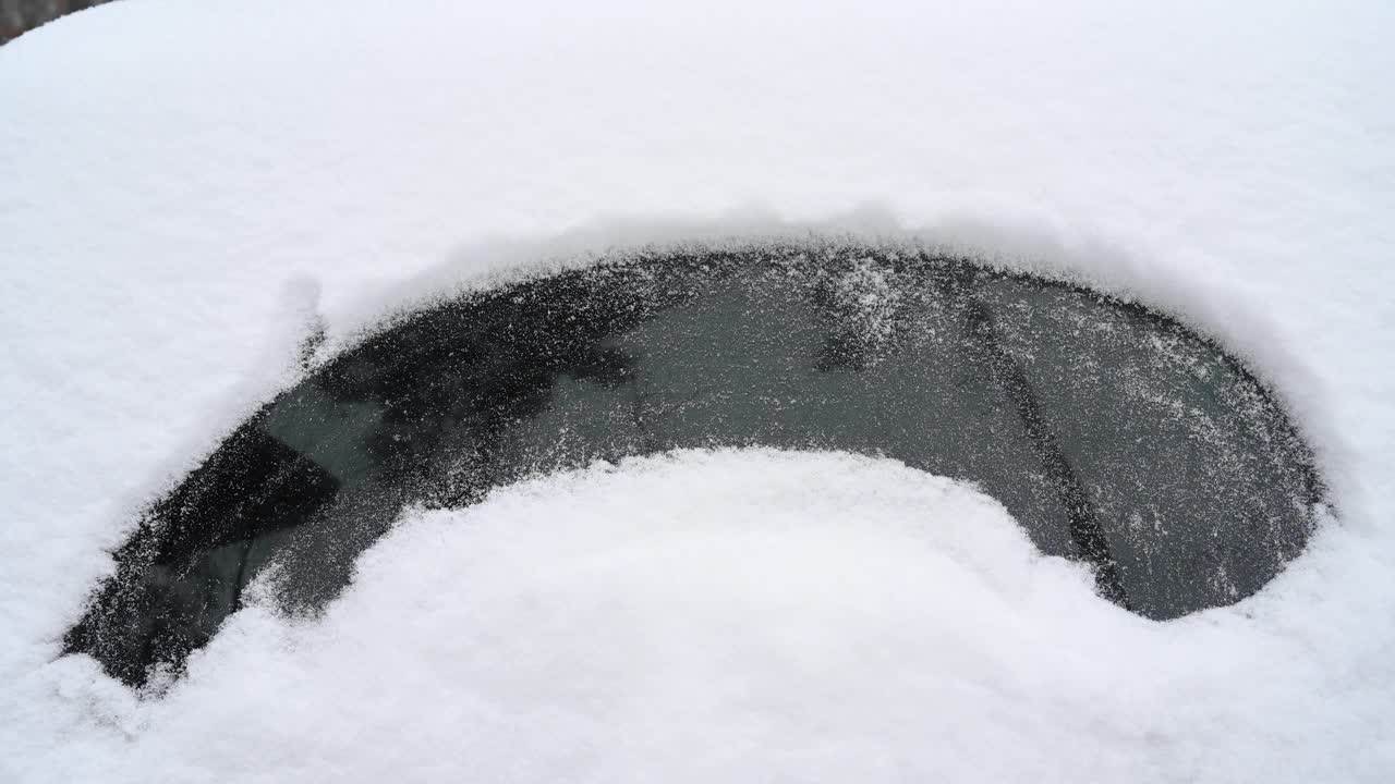 一名男子在一辆被暴风雪完全覆盖的汽车玻璃上画了一张眼睛的脸。德国。视频素材