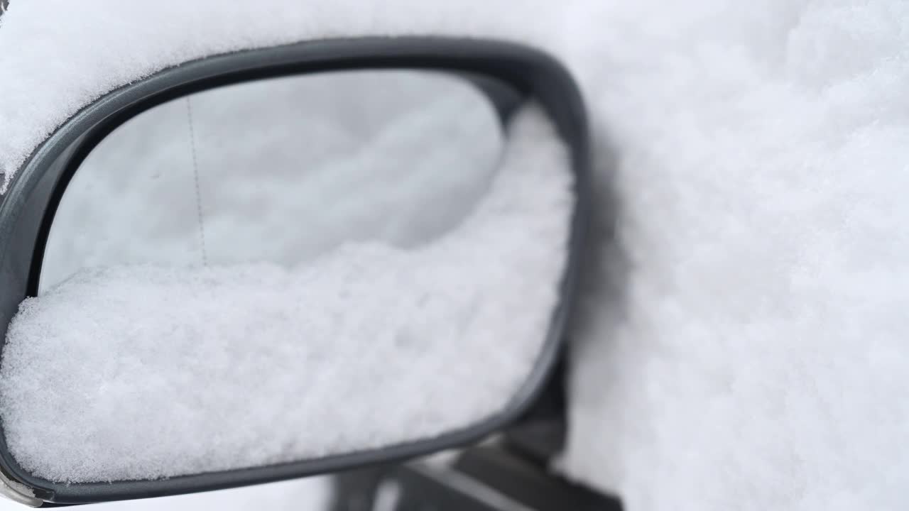 一个人在一个被雪覆盖的汽车后视镜前举着一个红色的心形图案。视频素材