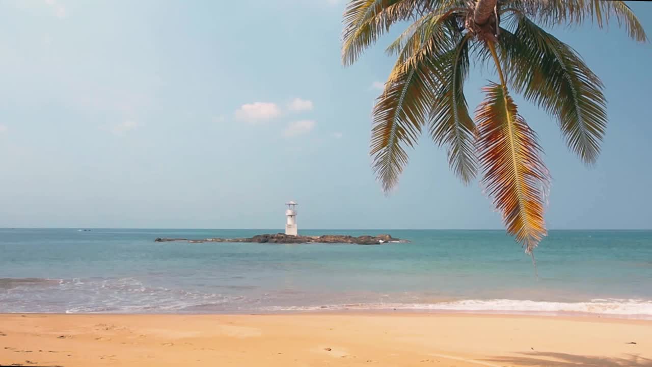 在阳光明媚的夏天去热带沙滩旅行。宽阔的沙滩上有椰子树和白色的小灯塔。蓝天上飘过缕缕云。阳光照在水面上。视频素材