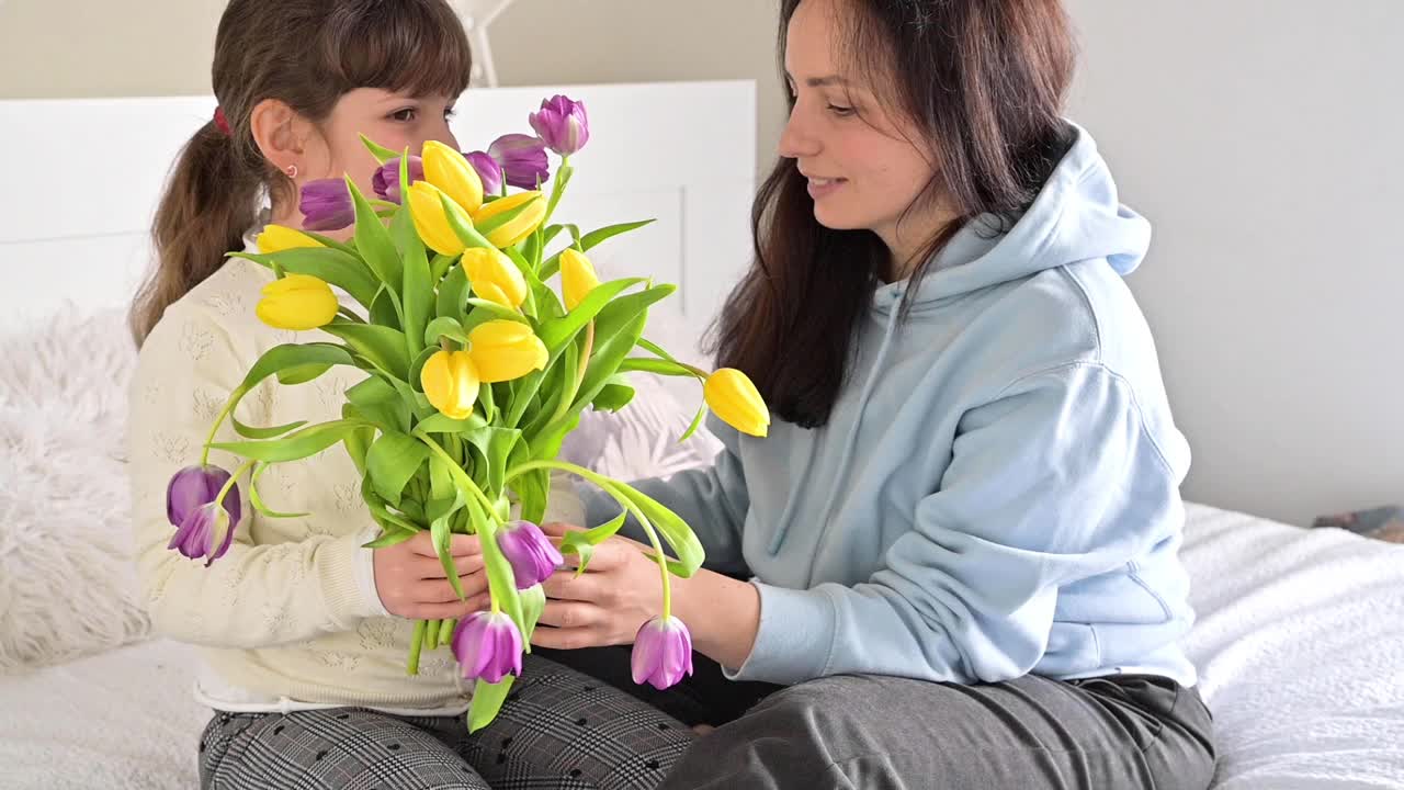 一个小女孩送给妈妈一束黄色和紫色的郁金香。母亲节，给女儿和妈妈一个深情的拥抱。3月8日给妈妈的礼物。视频素材