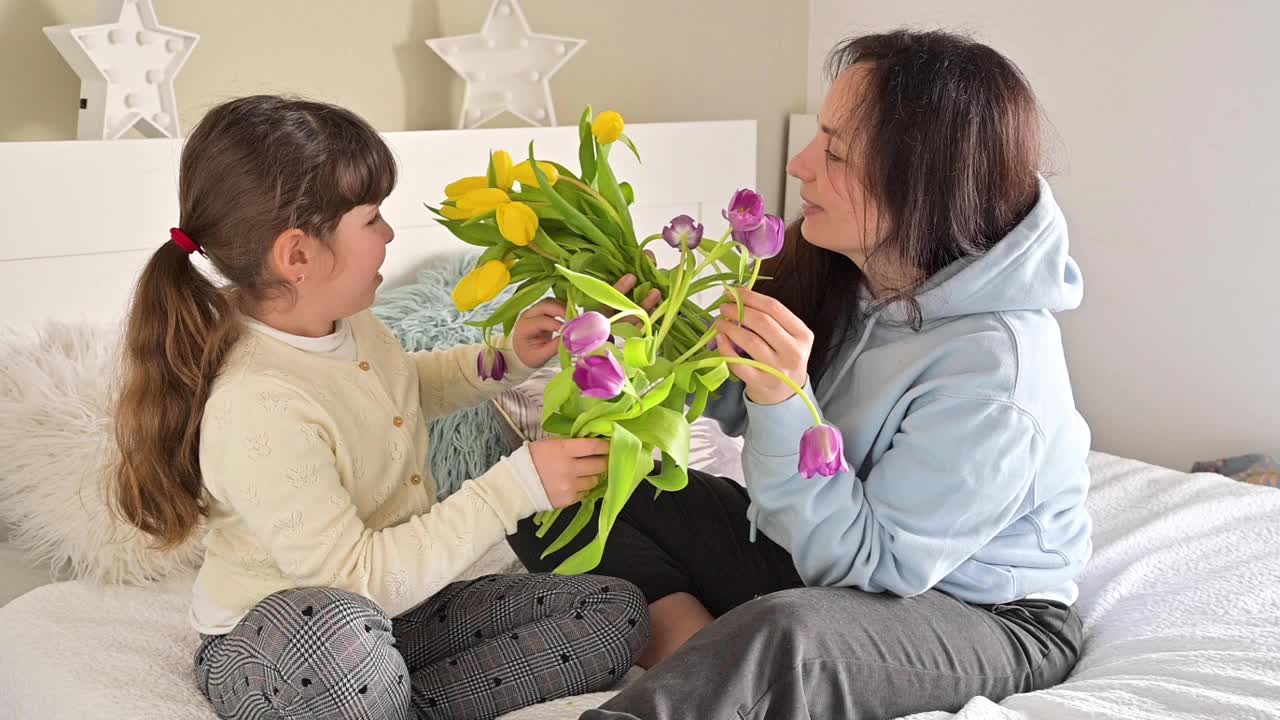 一个小女孩送给妈妈一束黄色和紫色的郁金香。母亲节，给女儿和妈妈一个深情的拥抱。3月8日给妈妈的礼物。视频素材