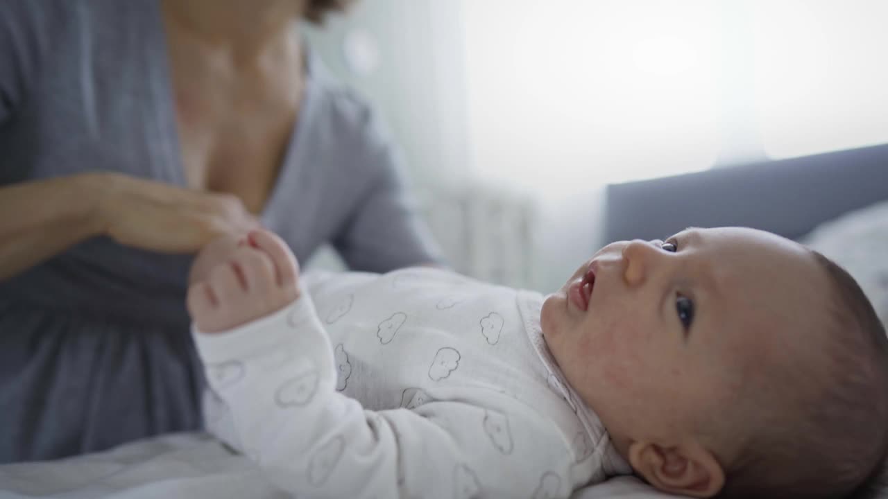 妈妈在家里的床上对着她可爱的小婴儿做体操视频素材