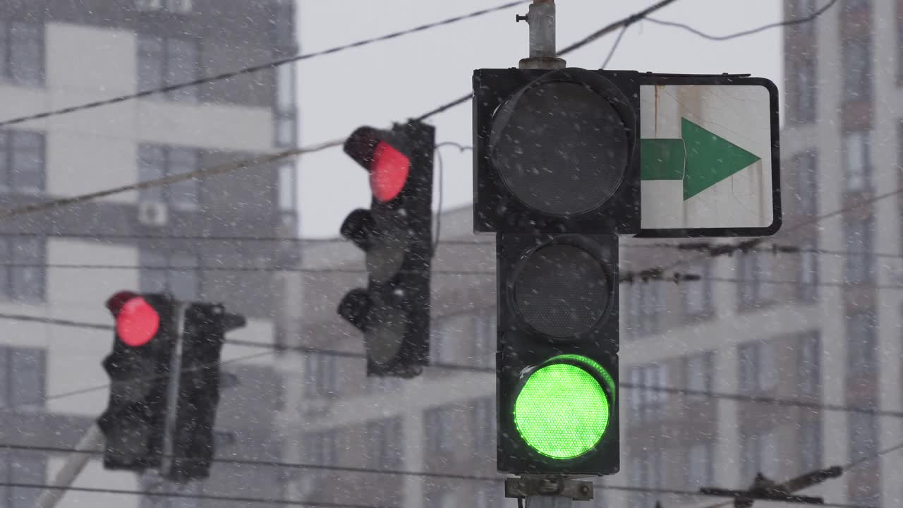 在一个下雪的冬日，城市街道上的交通灯。特写镜头。绿色变暗，红色变亮。暴风雪期间的道路交通。在困难的道路条件下的驾驶安全视频素材