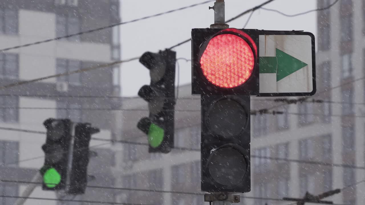 在一个下雪的冬日，城市街道上的交通灯。特写镜头。红色变暗，绿色变亮。暴风雪期间的道路交通。在困难的道路条件下的驾驶安全视频素材