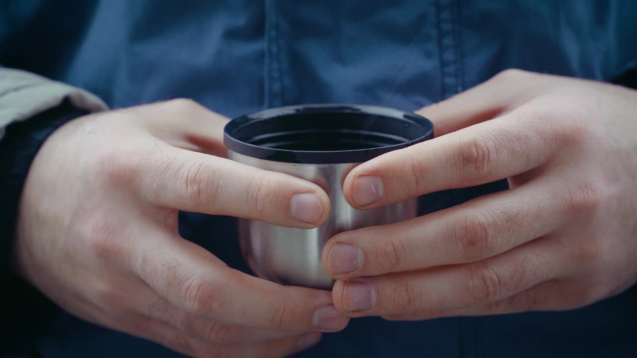 游客与旅客的手与金属马克杯的靠近。徒步旅行者与热杯茶或咖啡在暴风雪中在中性背景视频素材