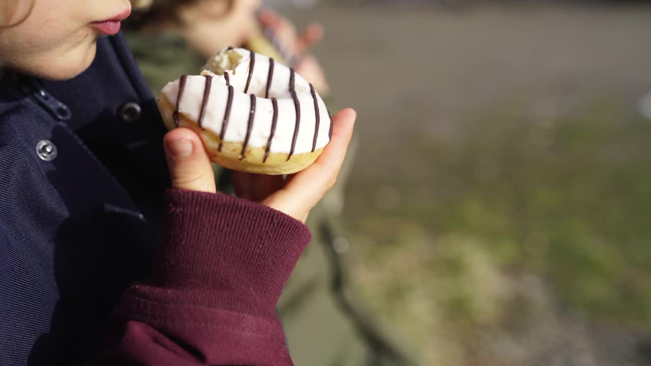 两个孩子坐在长凳上吃甜甜圈视频素材