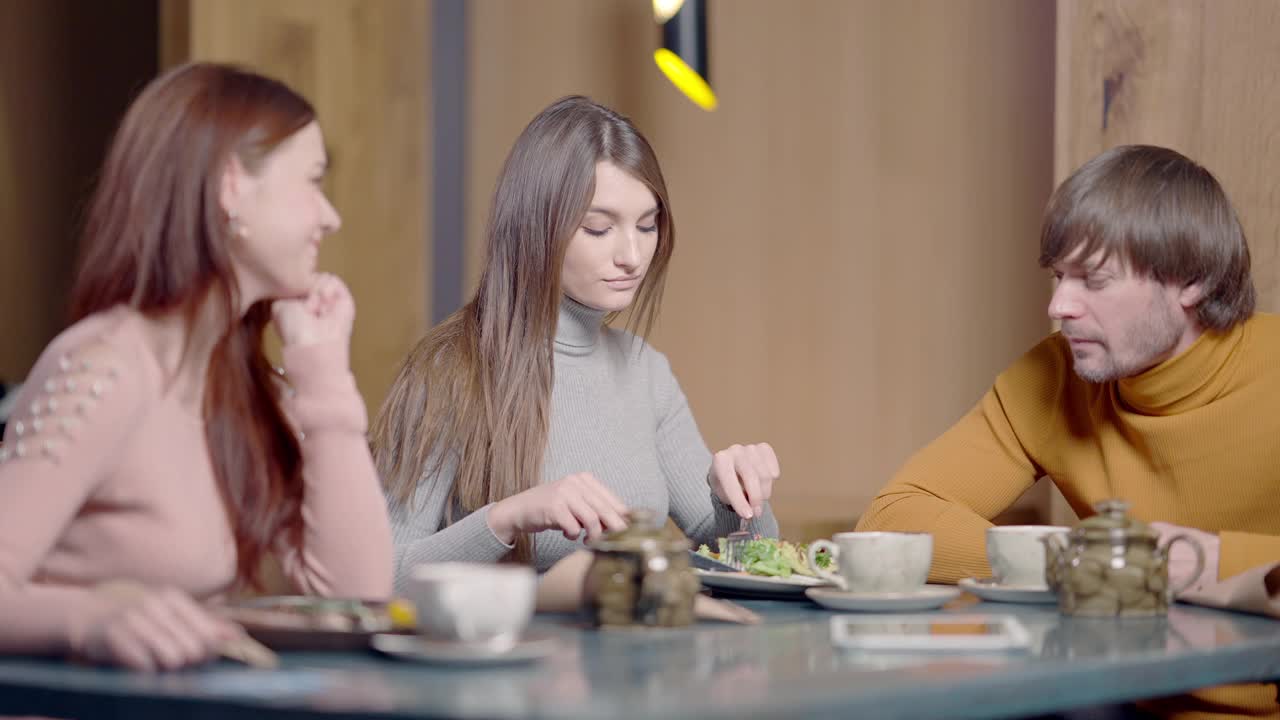 年轻女子吃着美味的牛排，像朋友一样坐在餐馆的桌子上聊天。自信的白人男人和女人在午餐时间聊天和微笑。缓慢的运动。视频素材