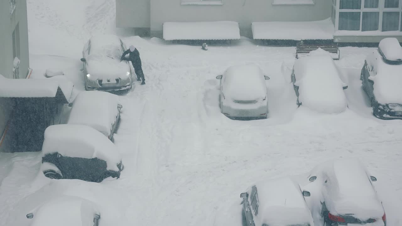 俯视图，一名男子清理停在雪地附近的一辆汽车。大雪视频素材