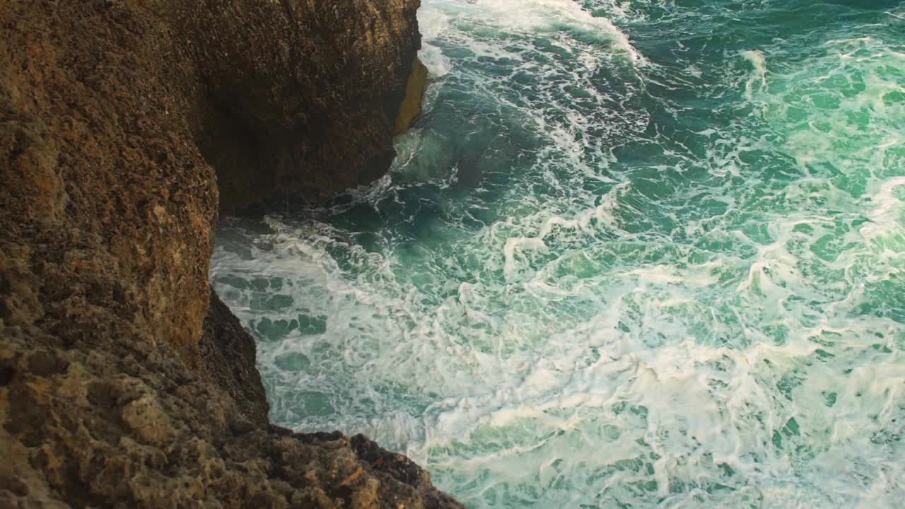 海浪拍打着岩石海岸，绿色的水溅起浪花，产生白色的泡沫，从上面看，慢动作视频视频素材