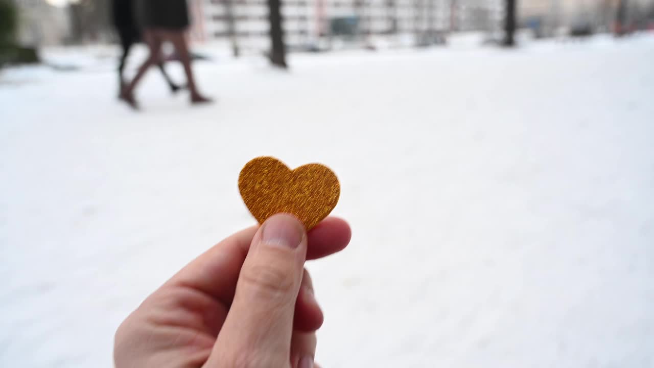 一个正在运动的人举着一个红色的心形在一个下雪的街道在城市。一对模糊的情侣在背景中行走。德国柏林。视频素材