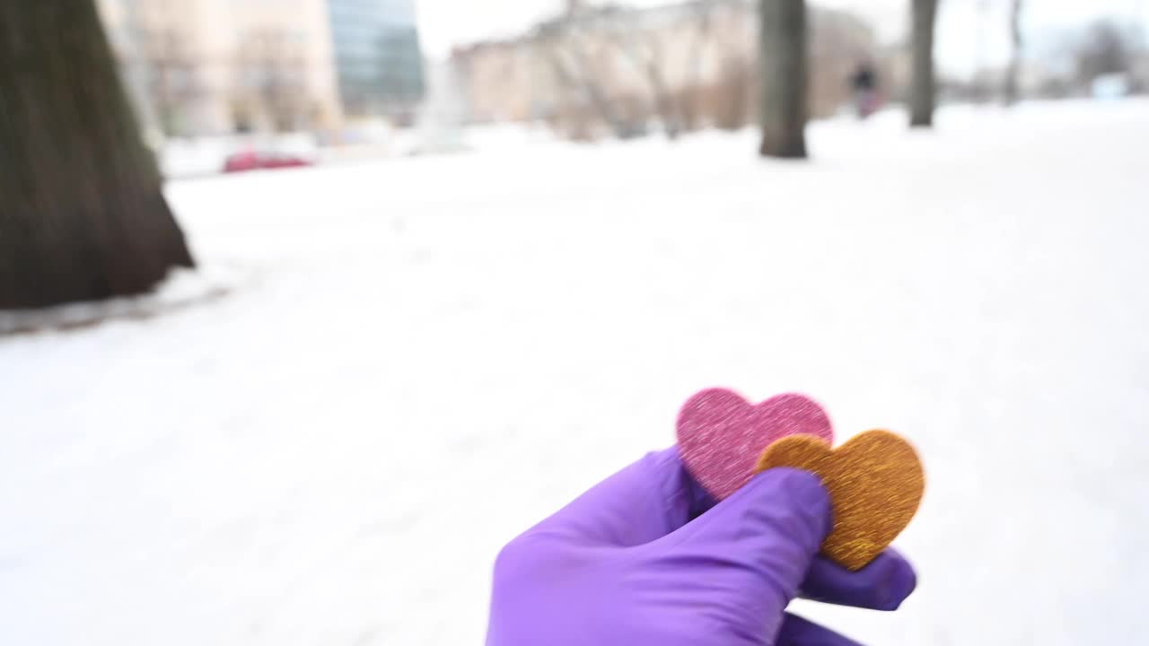 一个戴着橡胶手术手套的不可辨认的人在城市的一条积雪的街道上举着两个心形。德国柏林。视频素材