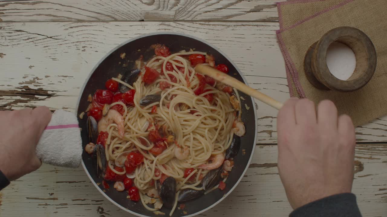 俯视图烹饪意大利面与datterini，西红柿与油炸大蒜和海鲜在一个烹饪锅视频素材