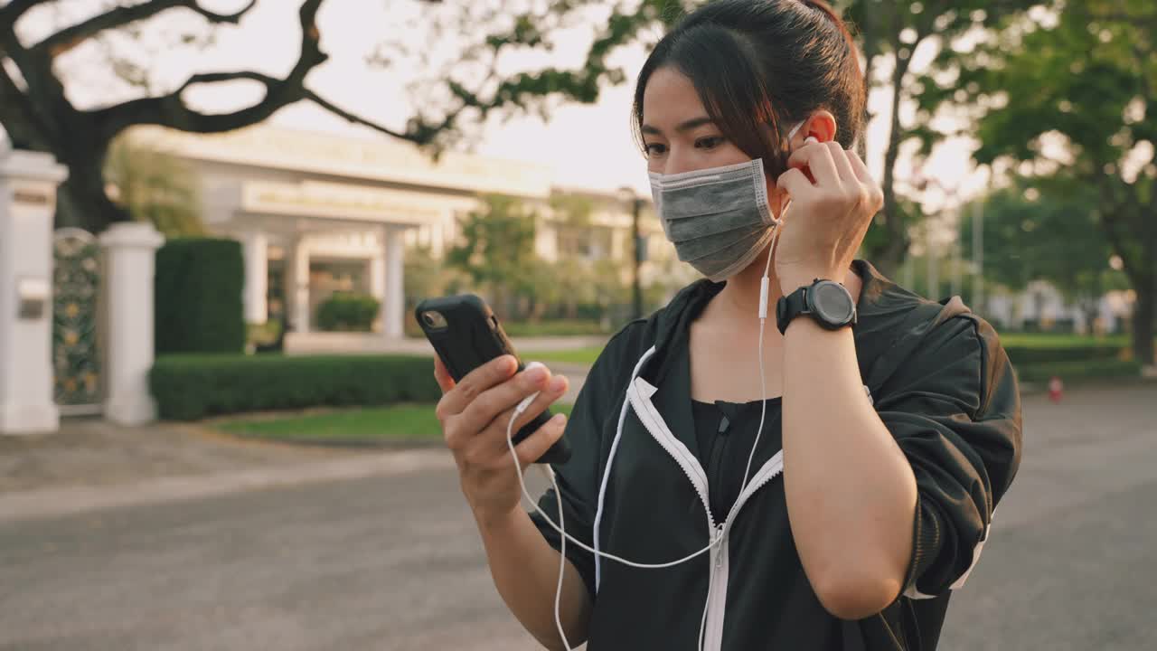 跑步的女人准备跑步，并开始在日落时分在公园里跑步，戴着耳机听着音乐。视频素材