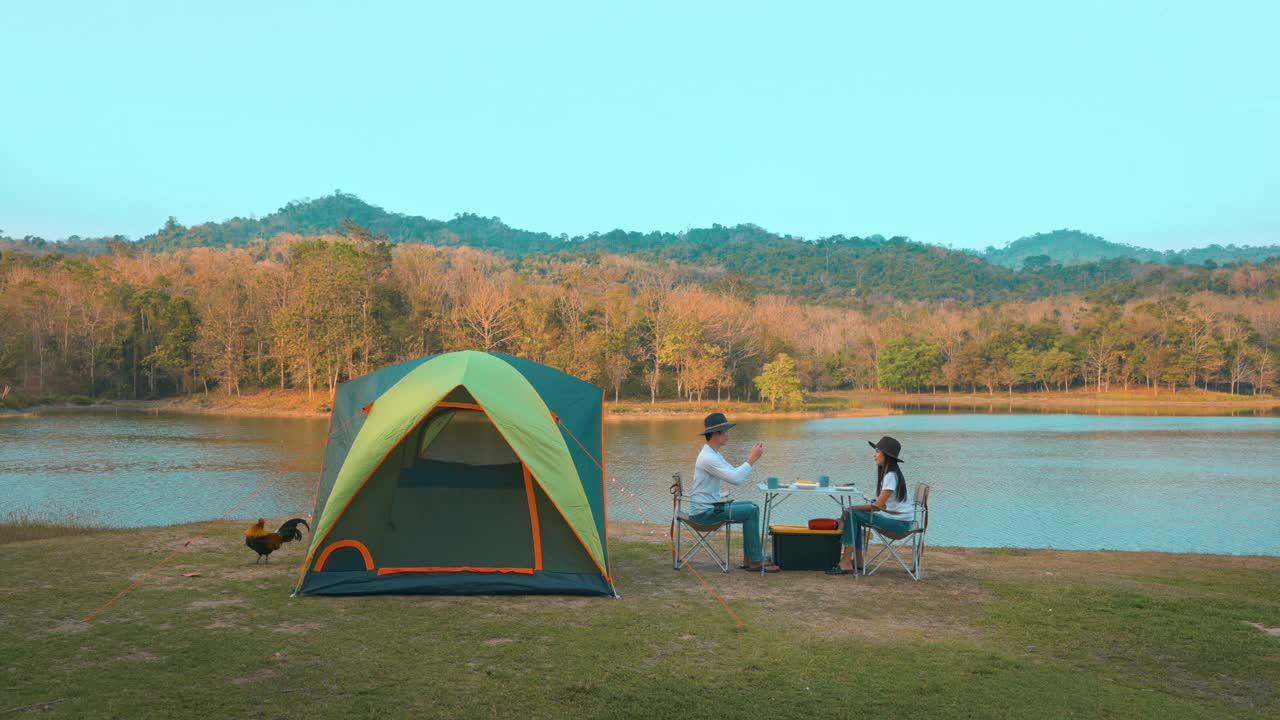 一对旅行情侣在湖边和山景的露营中吃晚餐，旅游目的地，自然旅游概念。视频素材