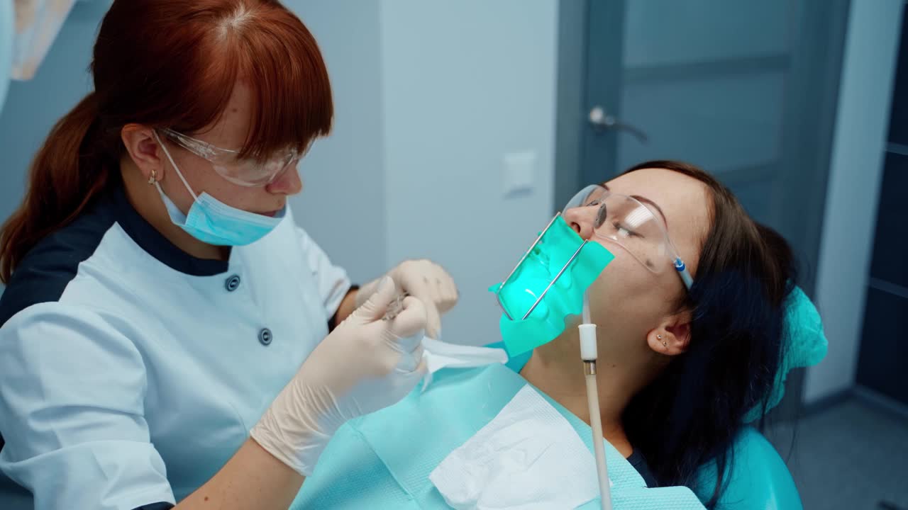 女病人在牙齿治疗期间牙痛。专业女牙医戴口罩和眼镜，在口腔诊所使用医疗器械治疗牙齿。视频素材