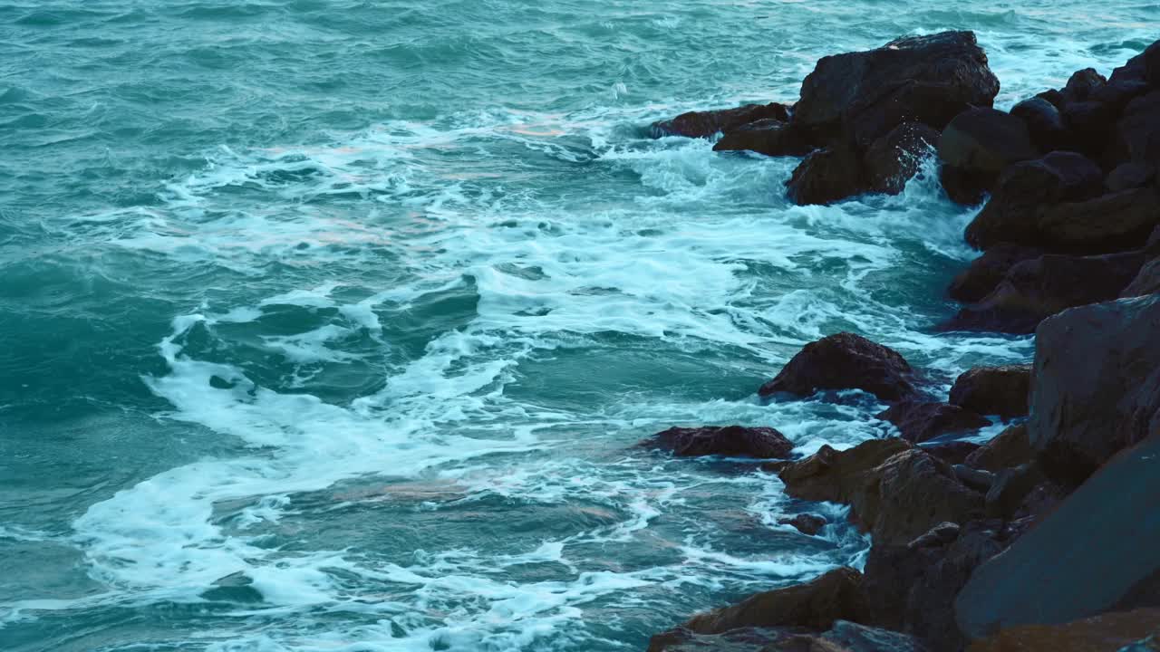 海水的浪花溅起泡沫溅向海岸的岩石，呈蓝色调视频素材