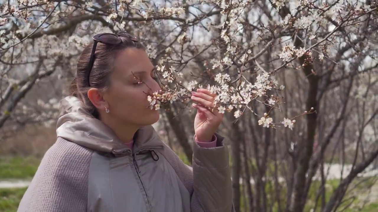 美丽的少女在春天的樱桃园里享受自然，快乐的美丽的少女在树木盛开的花园里。春天，树后的女人视频素材