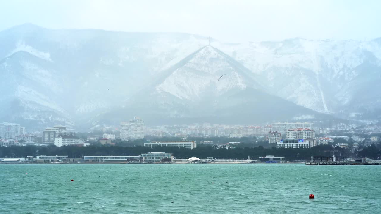 格伦齐克市在冬天的白雪皑皑的天气里，群山被白雪覆盖，海浪和风吹在海湾水面上，没有人在城市中行走视频素材