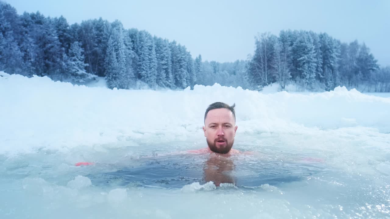 冬天游泳，治疗感冒。年轻人在冰水中游泳，背景是白雪覆盖的森林视频素材