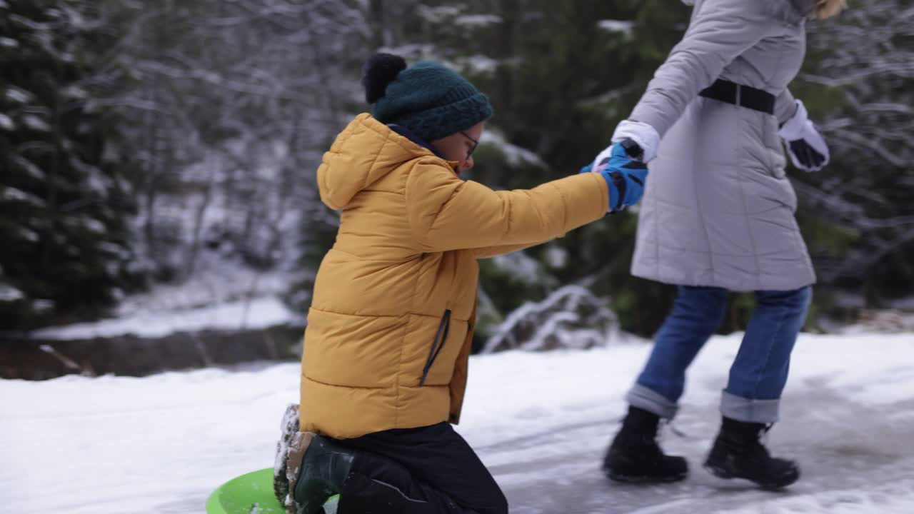 在冬天的一天，母亲拉着她的儿子在雪橇上视频素材