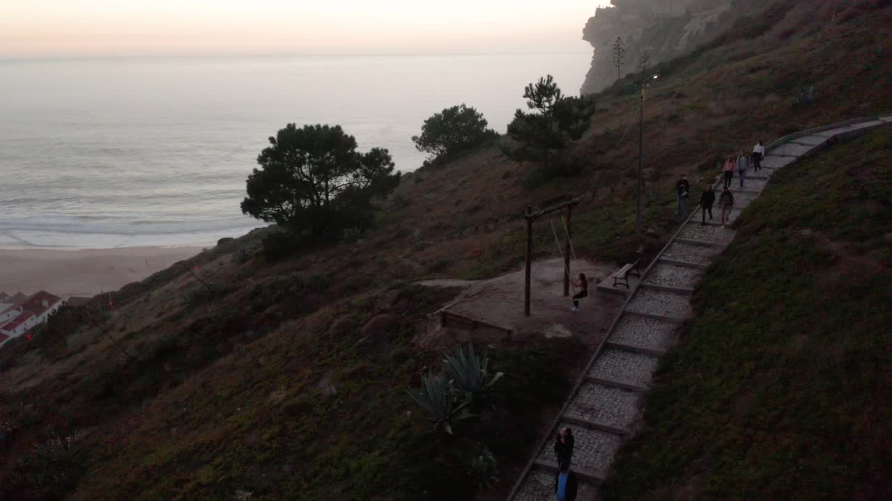 游客在山上的步道俯瞰小镇和海滩在葡萄牙的纳扎尔视频素材