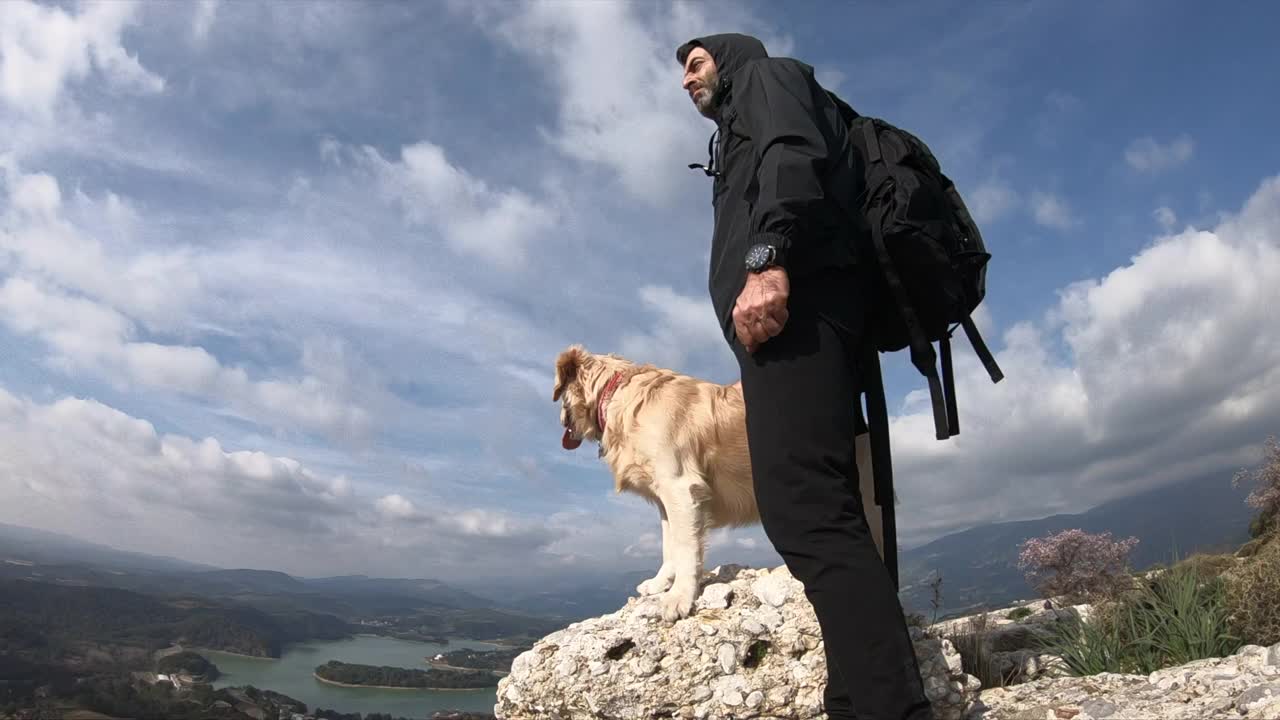 一个徒步旅行者和他的狗站在山顶上。视频素材