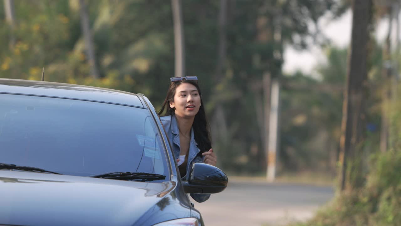 亚洲妇女在她的朋友开车时，在车外举起并示意她的手;慢动作视频素材