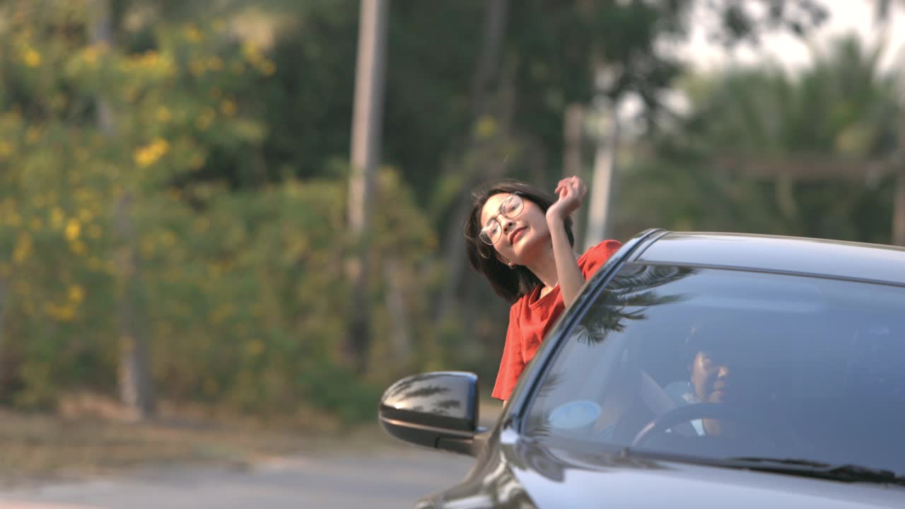 亚洲妇女在她的朋友开车时，在车外举起并示意她的手;慢动作视频下载