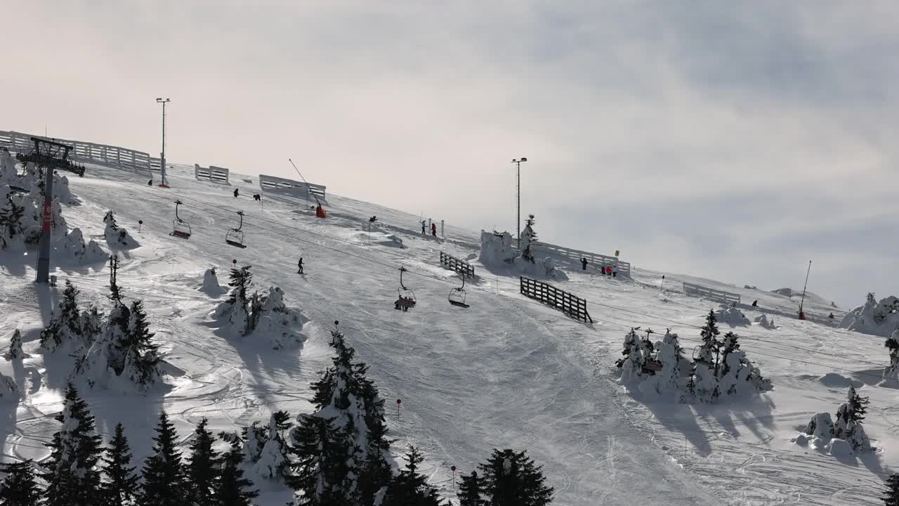 在阴天的冬季，在索道上移动的升降机和在滑雪道上滑雪的滑雪者视频素材