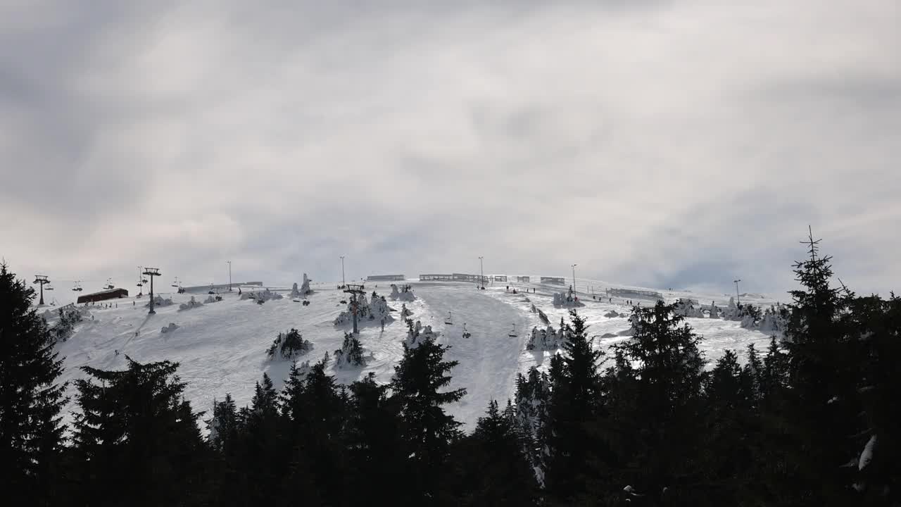 在阴天的冬季，在索道上移动的升降机和在滑雪道上滑雪的滑雪者视频素材