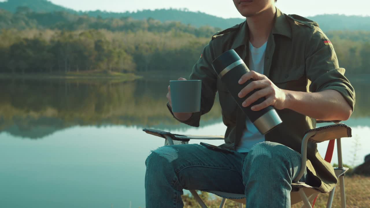 近距离的一个旅行者正在喝热咖啡越过山和河的观点，露营的概念，自然旅游。视频素材