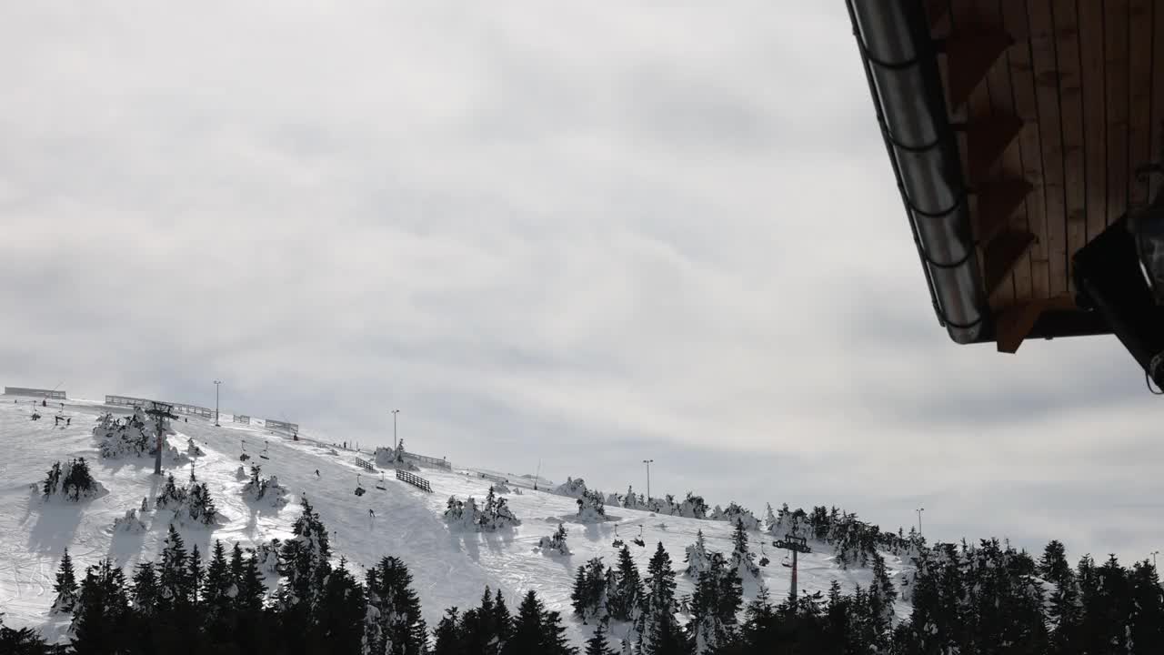 在阴天的冬季，在索道上移动的升降机和在滑雪道上滑雪的滑雪者视频素材