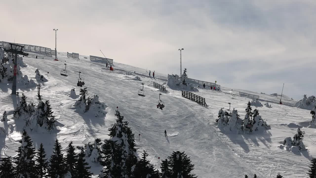 在阴天的冬季，在索道上移动的升降机和在滑雪道上滑雪的滑雪者视频素材