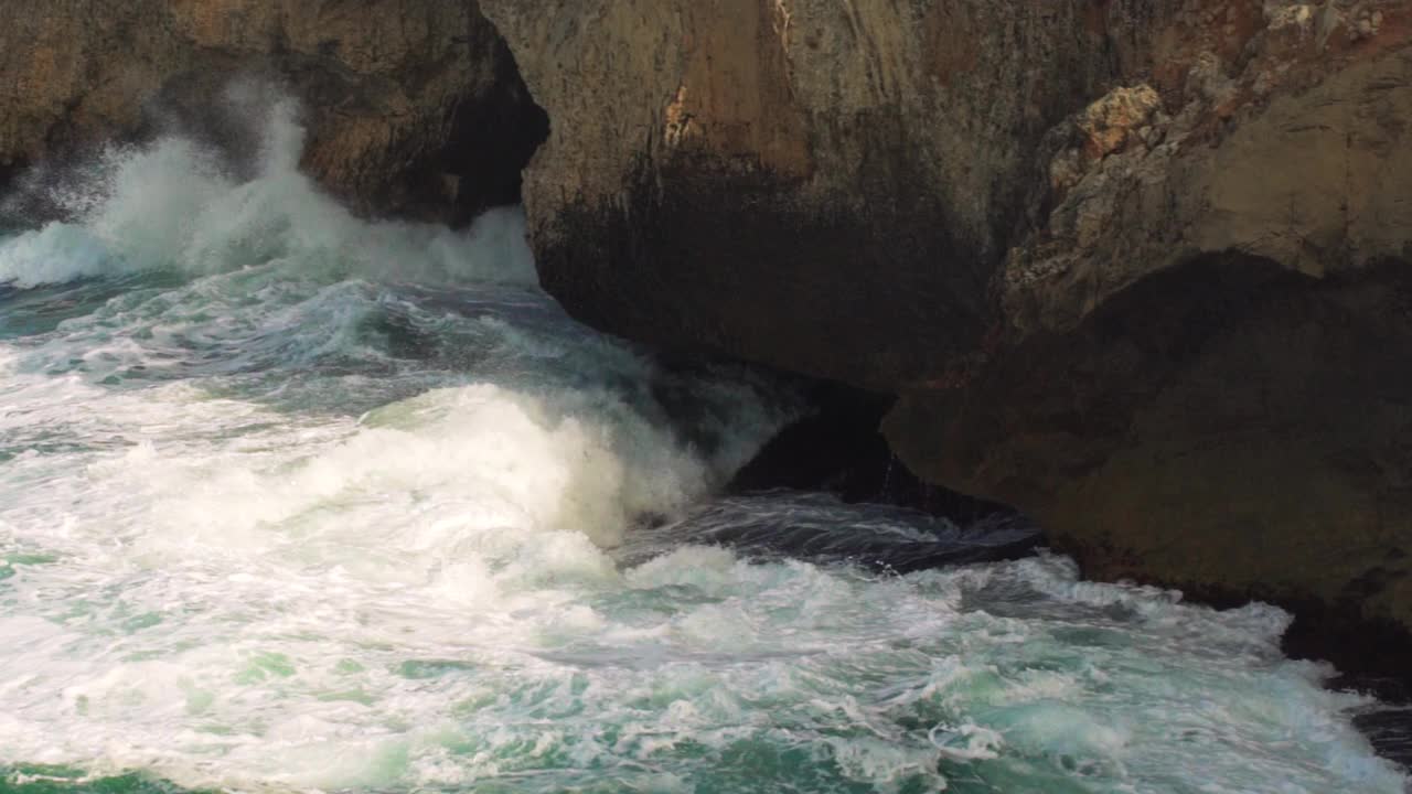 海浪拍打着岩石海岸，绿色的水溅起浪花，产生白色的泡沫，从上面看，慢动作视频视频素材