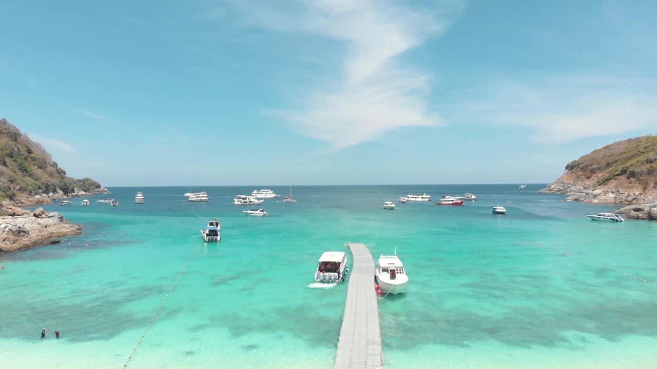 在泰国普吉岛外的Ko Racha Yai岛上，木制码头穿过干净的绿松石海，挤满了游客的游艇和渔船视频素材