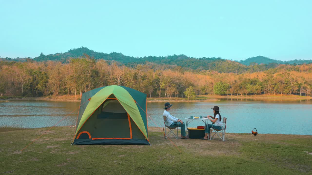 一对旅行情侣在湖边和山景的露营中吃晚餐，旅游目的地，自然旅游概念。视频素材