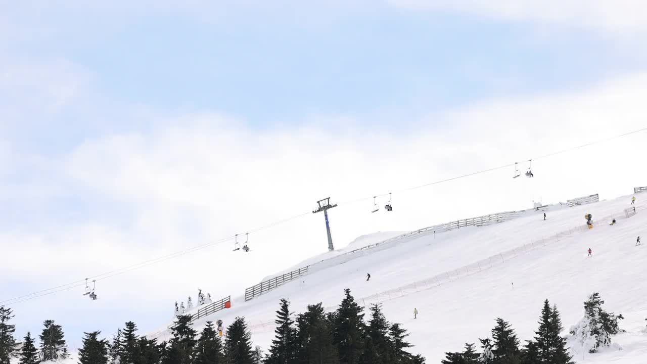 在阳光明媚的冬日，可在索道上升降的升降机及在斜坡上滑雪的滑雪者视频素材